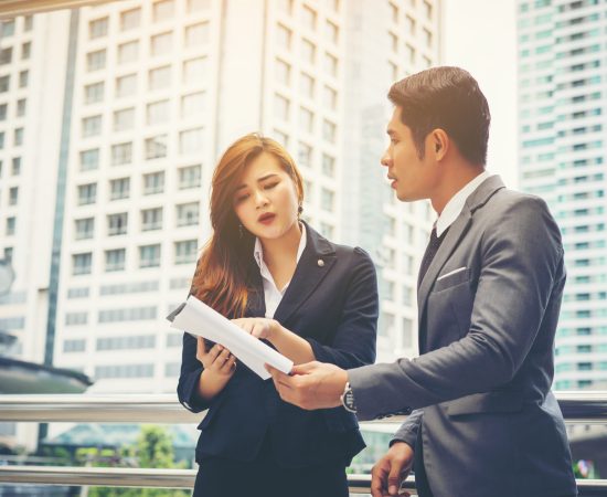 business-man-pointing-document-with-smile-discussing-something-with-her-coworker-while-standing-front-office-scaled.jpg